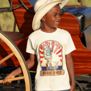 Child wearing youth graphic tee with Rodeo owl logo in front of a carriage.